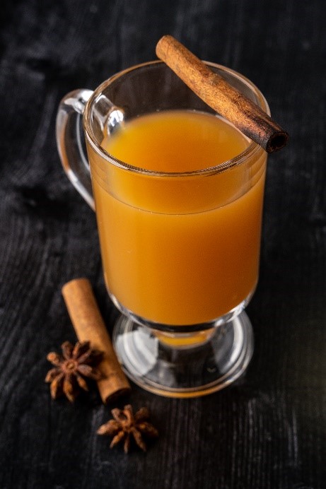 A glass of orange liquid with a cinnamon stick and anise

Hot Cider