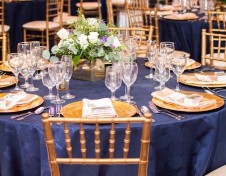 Elegant gala table setting featuring royal blue tablecloths, gold Chiavari chairs, and stunning floral centerpieces